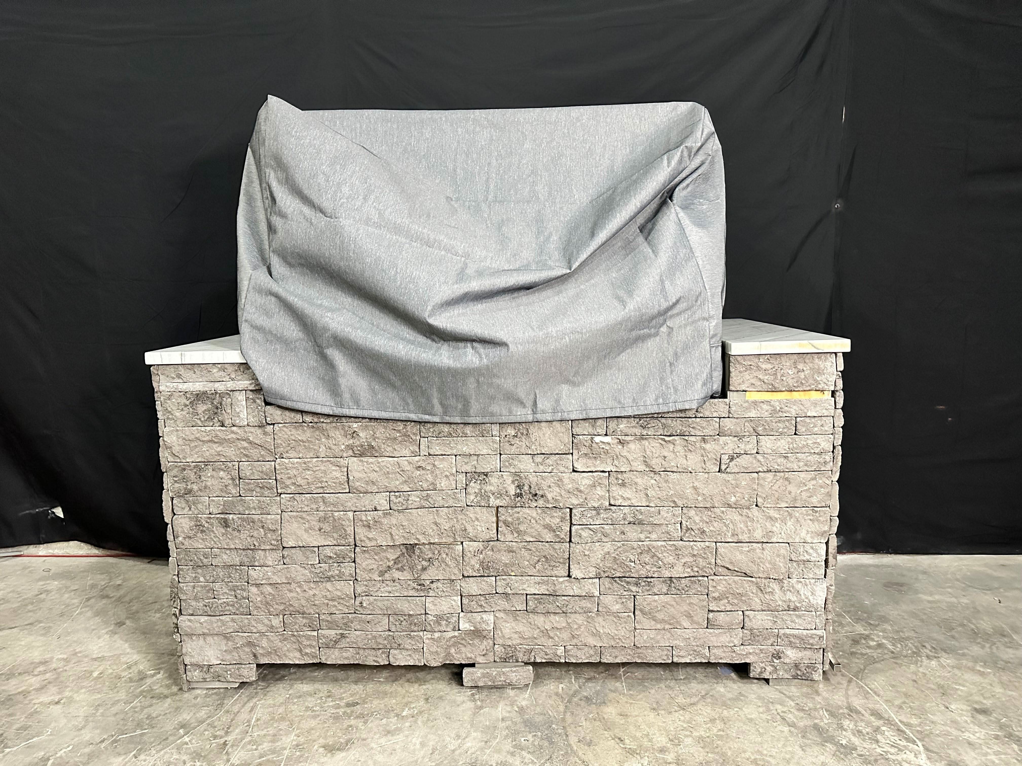 A grey fabric cover on a built-in outdoor grill in a stone base -smokeforges