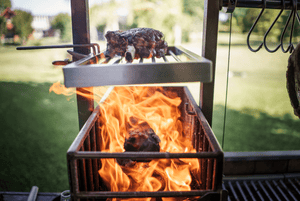 A large piece of meat cooking on an outdoor wood-fired grill over hot flames -smokeforges