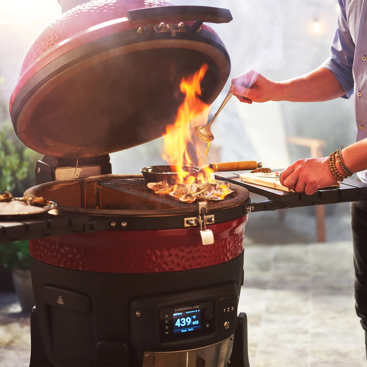 Red kamado grill with flames and a person cooking outdoors