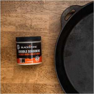 Blackstone Griddle Seasoning and Cast Iron Conditioner — container beside cast iron cookware